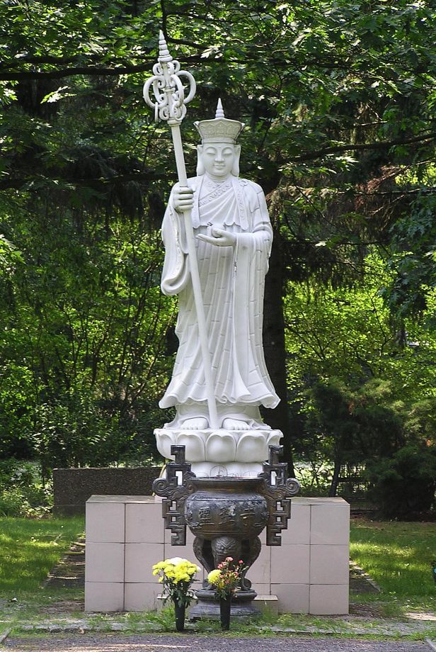 White Buddhist statue with a staff and incense burner at Ruhleben Cemetery
