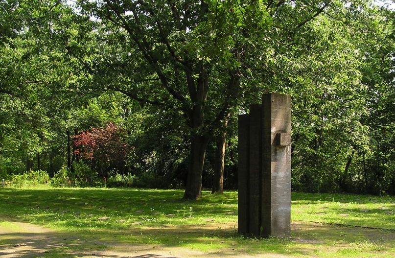 Stone memorial of three upright steles beneath trees at Ruhleben Cemetery